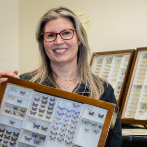 Woman smiling with framed butterfly species